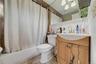 Beige tile wall and floor, white beadboard paneling, light wood-finish vanity, and a white bathtub