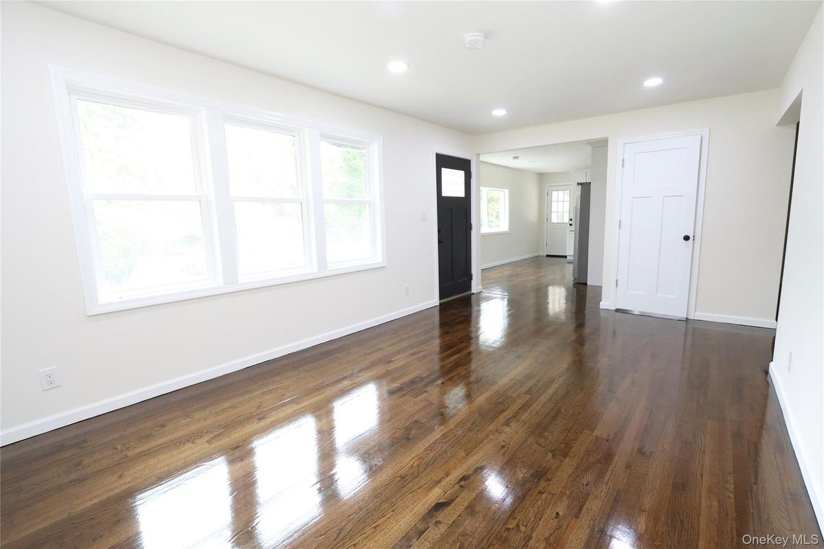 Spacious open living area showcasing refinished hardwood flooring, abundant natural light from triple-pane windows, recessed ceiling lighting, and cle