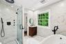 Glass-enclosed shower with matte black fixtures, freestanding soaking tub, and a window for natural illumination