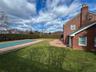 Brick exterior with a prominent chimney, a covered pool area, a paver patio, and mature perimeter hedging