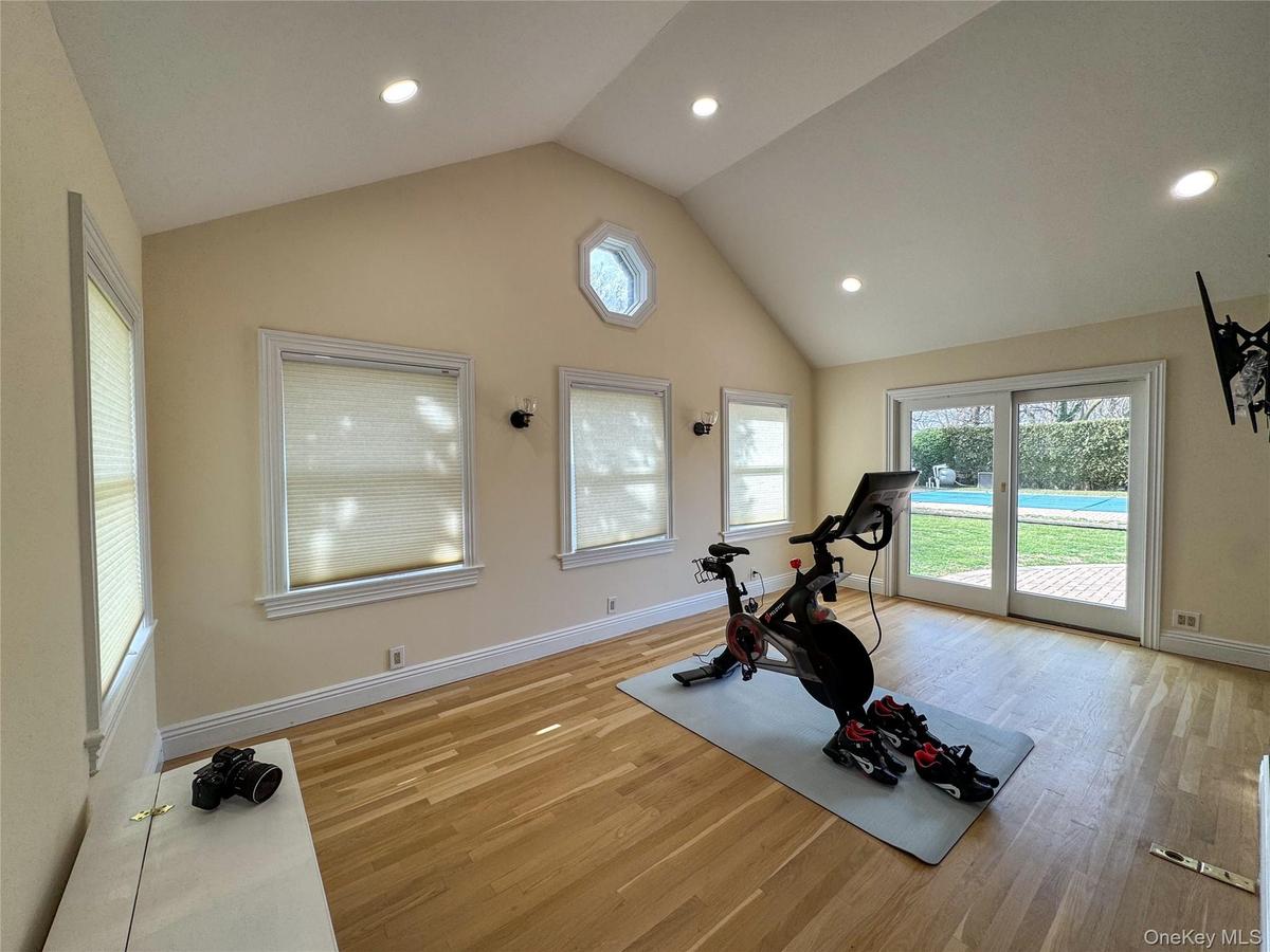Vaulted ceiling with recessed lighting, wood-finish flooring, multiple windows, and sliding glass doors opening to the exterior