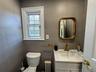 Gray tile walls, single hung window with white trim, white toilet, white vanity with integrated sink, brass-finish faucet