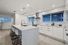 Spacious kitchen featuring a waterfall island, white flat-panel cabinetry, integrated stainless steel appliances, a stainless steel range hood, and re