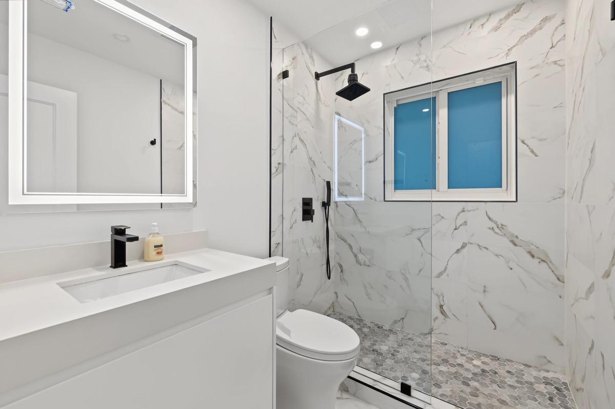 Vanity with integrated sink and matte black faucet, illuminated mirror, walk-in shower with glass enclosure, rain shower fixture, and hexagonal floor 