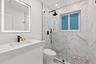 Vanity with integrated sink and matte black faucet, illuminated mirror, walk-in shower with glass enclosure, rain shower fixture, and hexagonal floor 