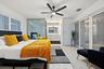 Room featuring a ceiling fan, white plantation shutters, glass partition, sliding opaque closet doors, and wood-finish flooring