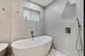 Freestanding soaking tub with brushed nickel fixtures, surrounded by large format wall tiling and a built-in window