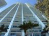 Contemporary high-rise building with a white exterior, multiple curved balconies, glass balcony railings, floor-to-ceiling windows, and surrounding pa