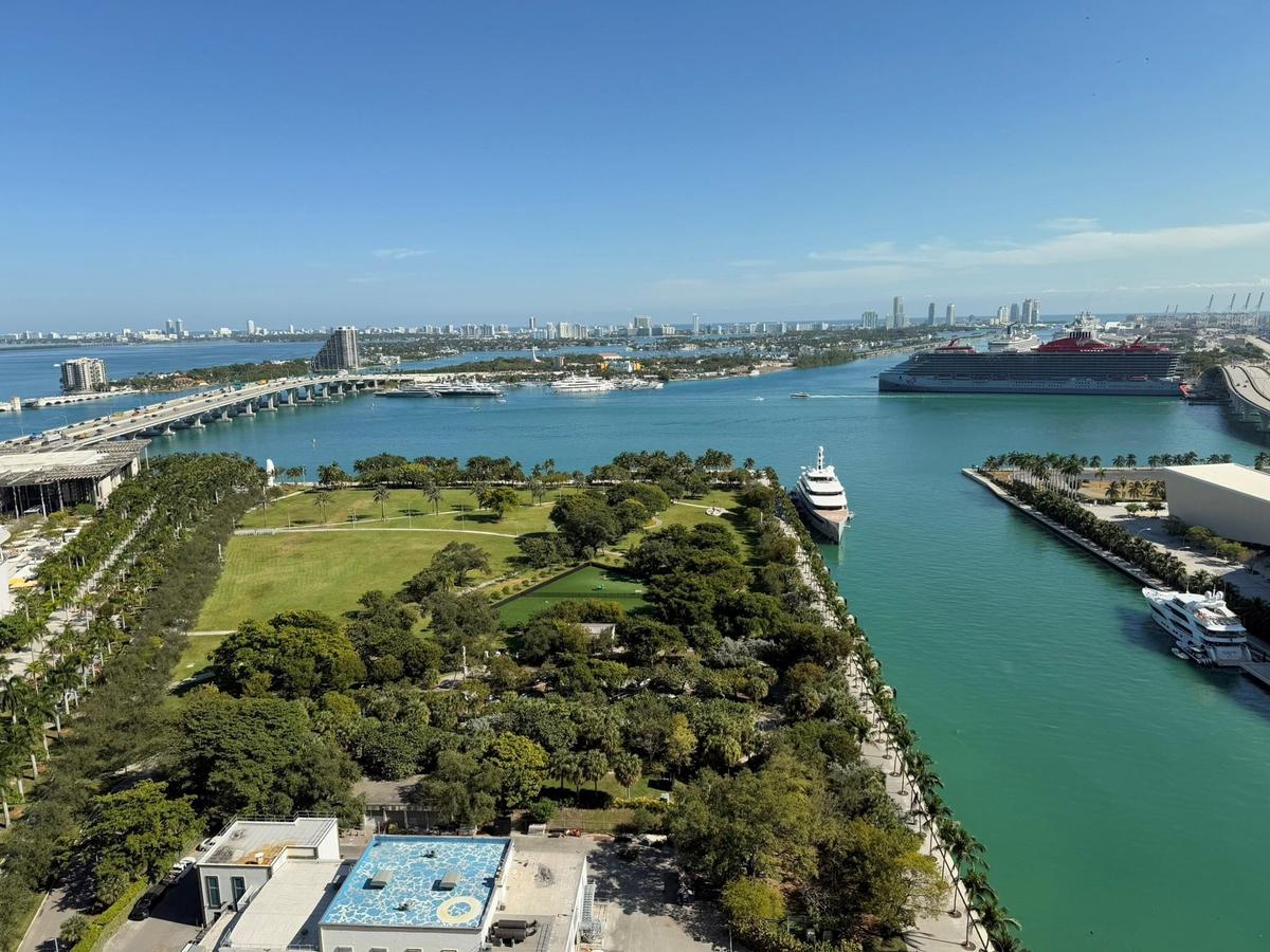 Expansive harbor and city skyline panorama featuring water views, a marine channel, lush parkland, and a distant bridge structure