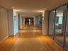 Expansive hallway featuring wood-finish flooring with alternating stone inlay, recessed ceiling lighting, and wall-mounted sconces