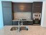 Kitchen featuring dark wood-finish cabinetry, integrated stainless steel appliances, a built-in cooktop, and speckled light-toned countertops