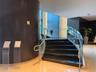 Curved staircase featuring dark treads and risers, clear glass railings, and a brushed metal handrail