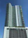 Contemporary high-rise building featuring a multi-story base, extensive window-lined facade, numerous private balconies, and a rooftop amenity deck wi