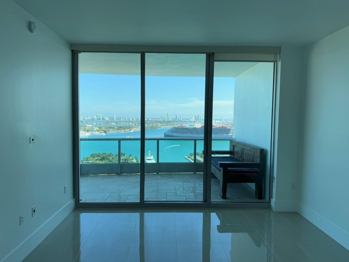 Floor-to-ceiling glass doors opening onto a private balcony with water and city skyline scenery