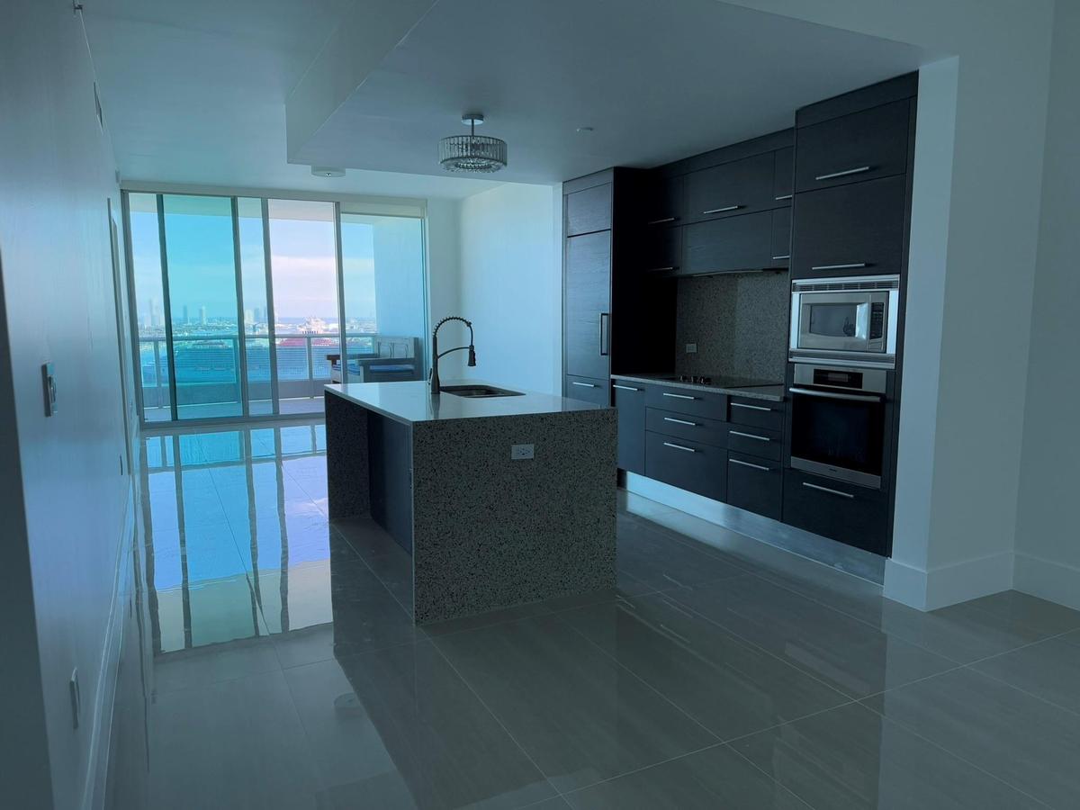Modern kitchen featuring dark cabinetry, stainless steel appliances, a large island with a sink, and polished tile flooring