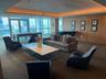 Expansive common area featuring a wall of floor-to-ceiling windows, wood-paneled walls, tray ceiling with cove lighting, and recessed ceiling lights