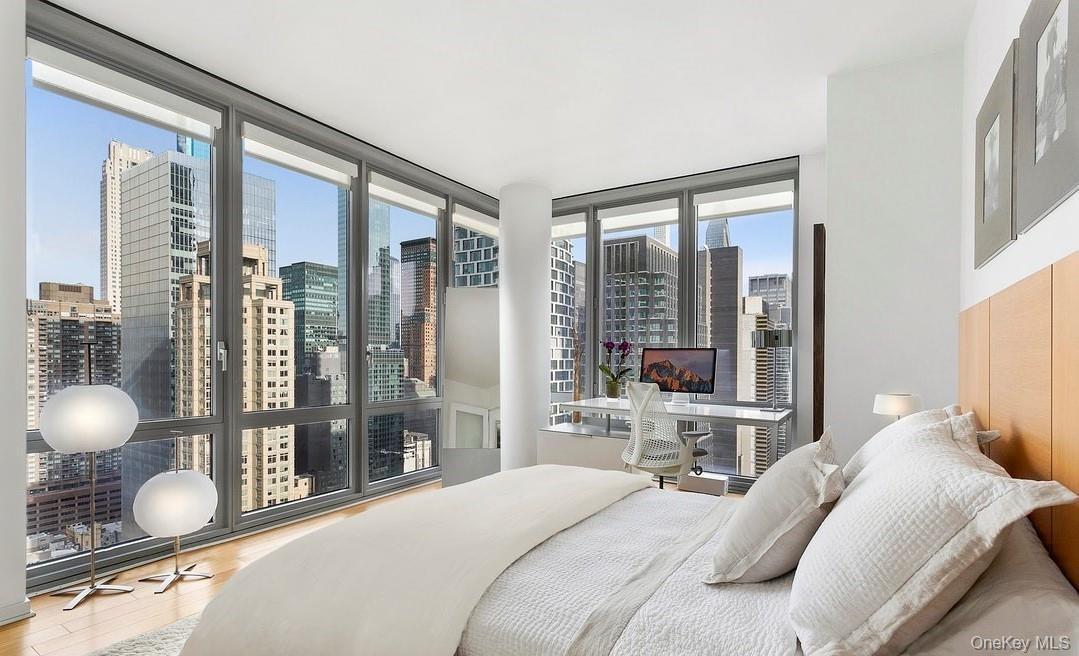 Bedroom with a wall of windows, wood finished floors, and a view of city