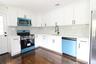 White cabinetry with matte black hardware, stone countertops, diamond pattern tile backsplash, and stainless steel appliances