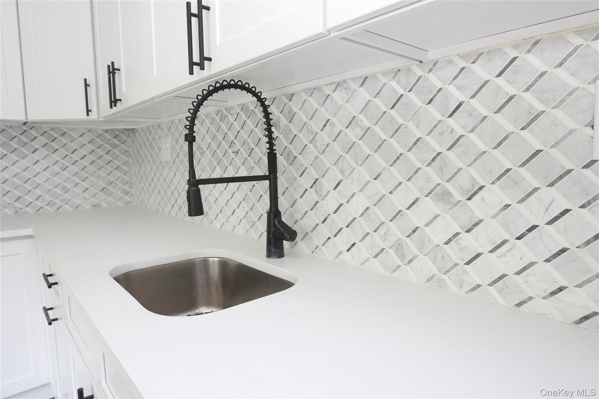 White cabinetry with matte black pulls, solid surface countertop, stainless steel undermount sink, matte black pull-down faucet, and geometric pattern
