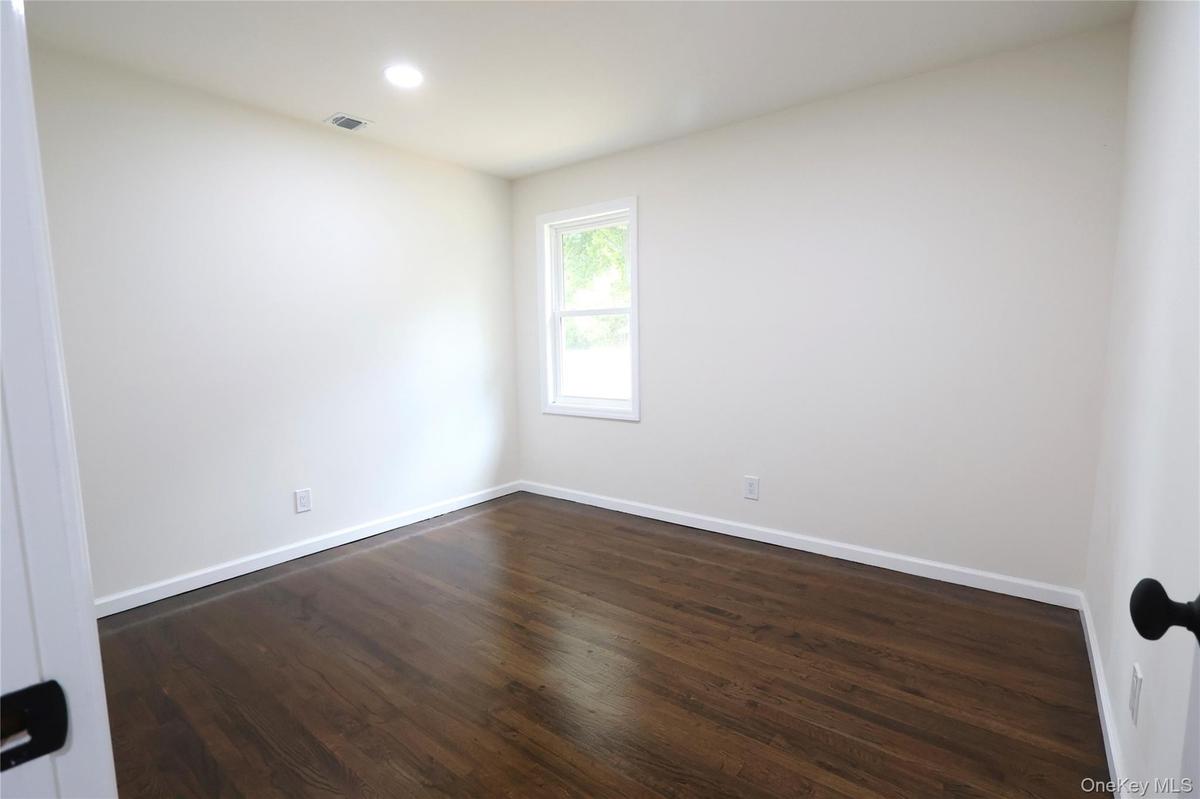 Recessed ceiling lighting illuminates wood-finish flooring and a single window with white trim