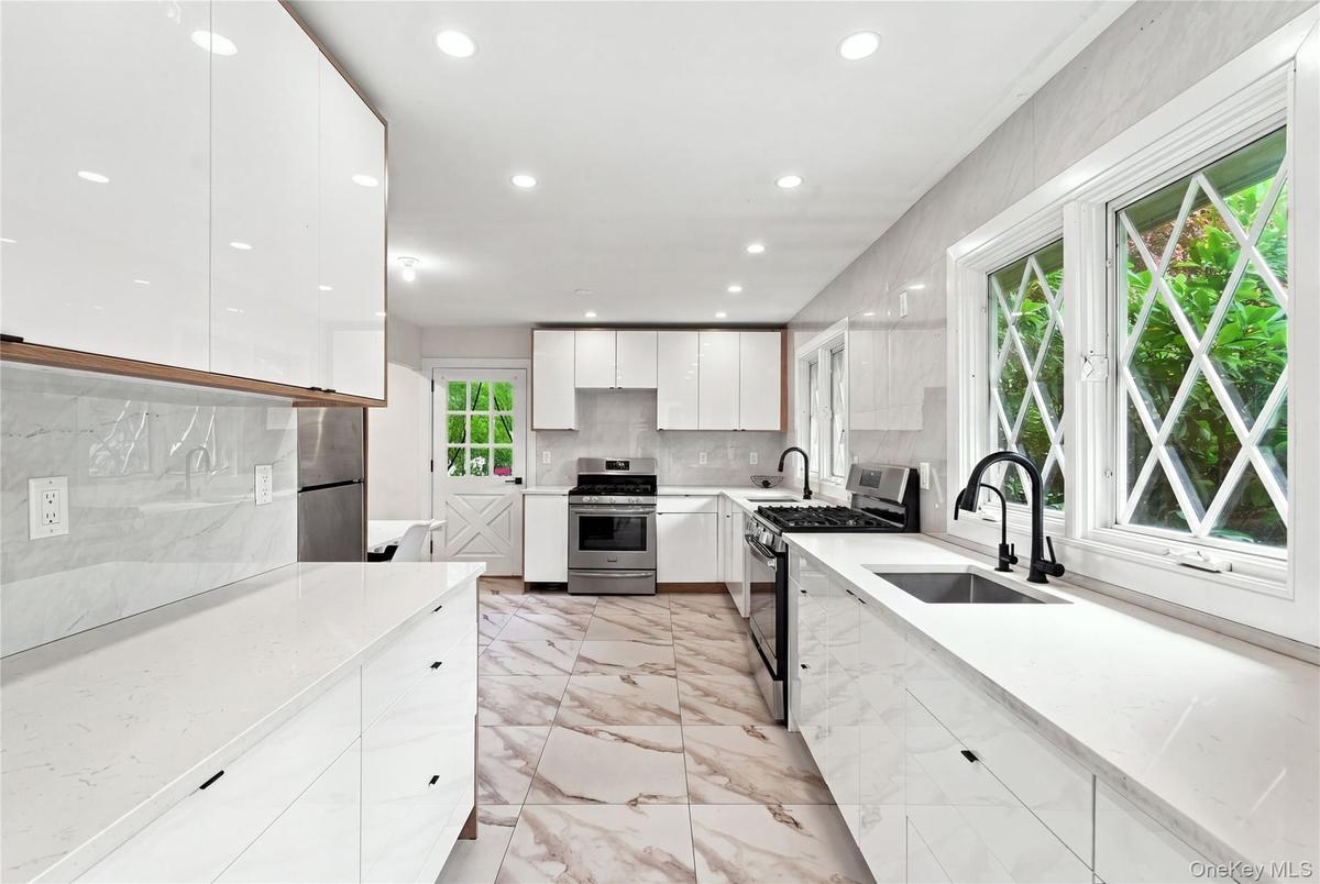 Kitchen featuring white flat-panel cabinetry, white countertops, stainless steel appliances, black fixtures, and patterned flooring