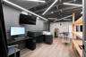 Recessed ceiling lighting, painted exposed ceiling joists, wood-finish flooring, built-in wooden shelving, and a wall-mounted display