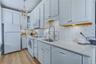 White kitchen cabinetry, stainless steel sink with a high-arc faucet, mosaic tile backsplash, light-colored countertops, and wood-finish flooring
