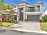 Modern elevation with clean architectural lines, lush landscaping, and an oversized paver driveway creating striking curb appeal.