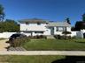 White siding exterior with a light gray shingle roof, paved driveway, and established front landscaping