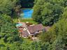 Tudor-style residence set amidst lush trees, featuring mahogany decking, stone patio, tennis court, and swimming pool.