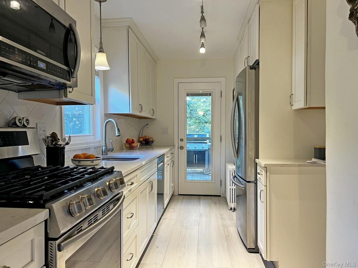 Kitchen with appliances with stainless steel finishes, pendant lighting, light stone counters, white cabinets, and light wood-style floors