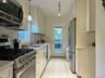 Kitchen with appliances with stainless steel finishes, pendant lighting, light stone counters, white cabinets, and light wood-style floors