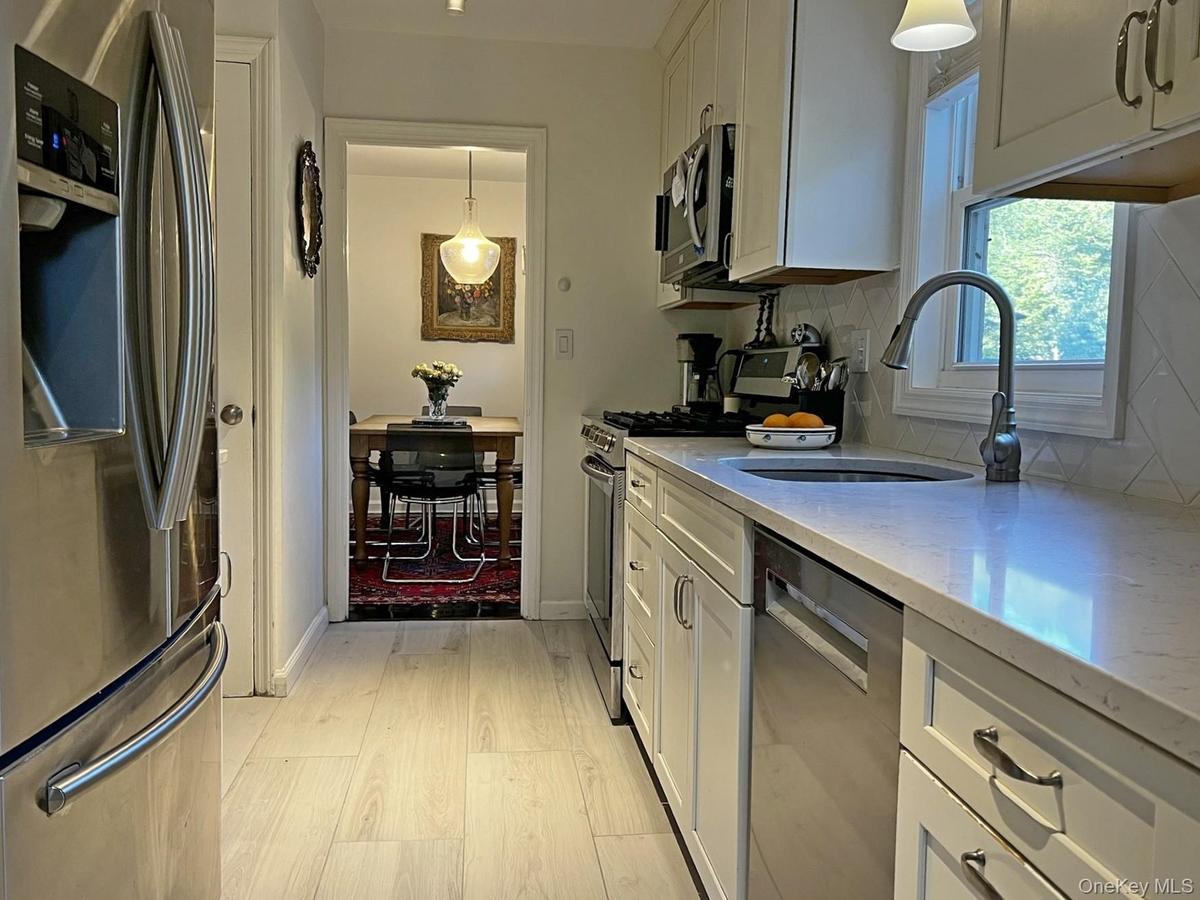 Kitchen featuring appliances with stainless steel finishes, decorative light fixtures, white cabinets, and light stone countertops