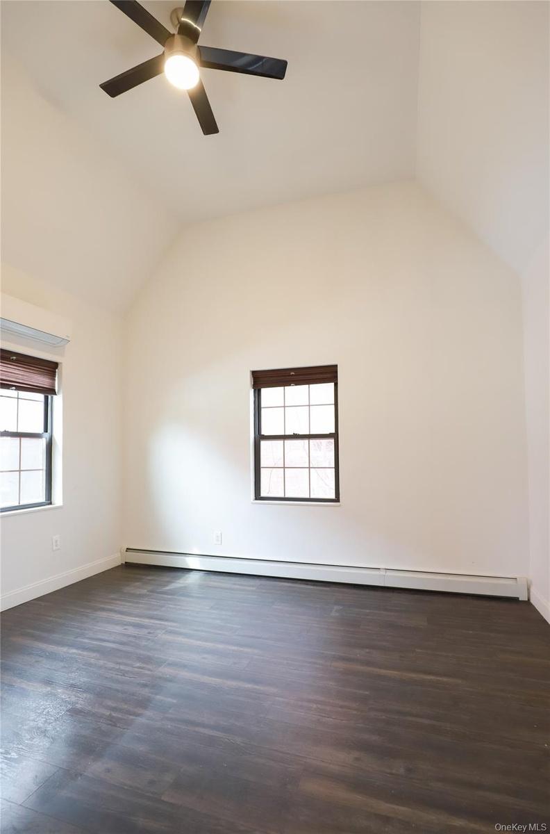 Vaulted ceiling, wood-finish flooring, two windows, two-tone blinds, and a ceiling fan with integrated lighting
