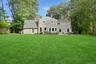 Expansive manicured lawn with mature trees, stone patio, built-in outdoor seating, and a stone fireplace