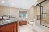 Dual vanity with dark stone countertop, glass-enclosed shower, built-in shower bench, and recessed lighting