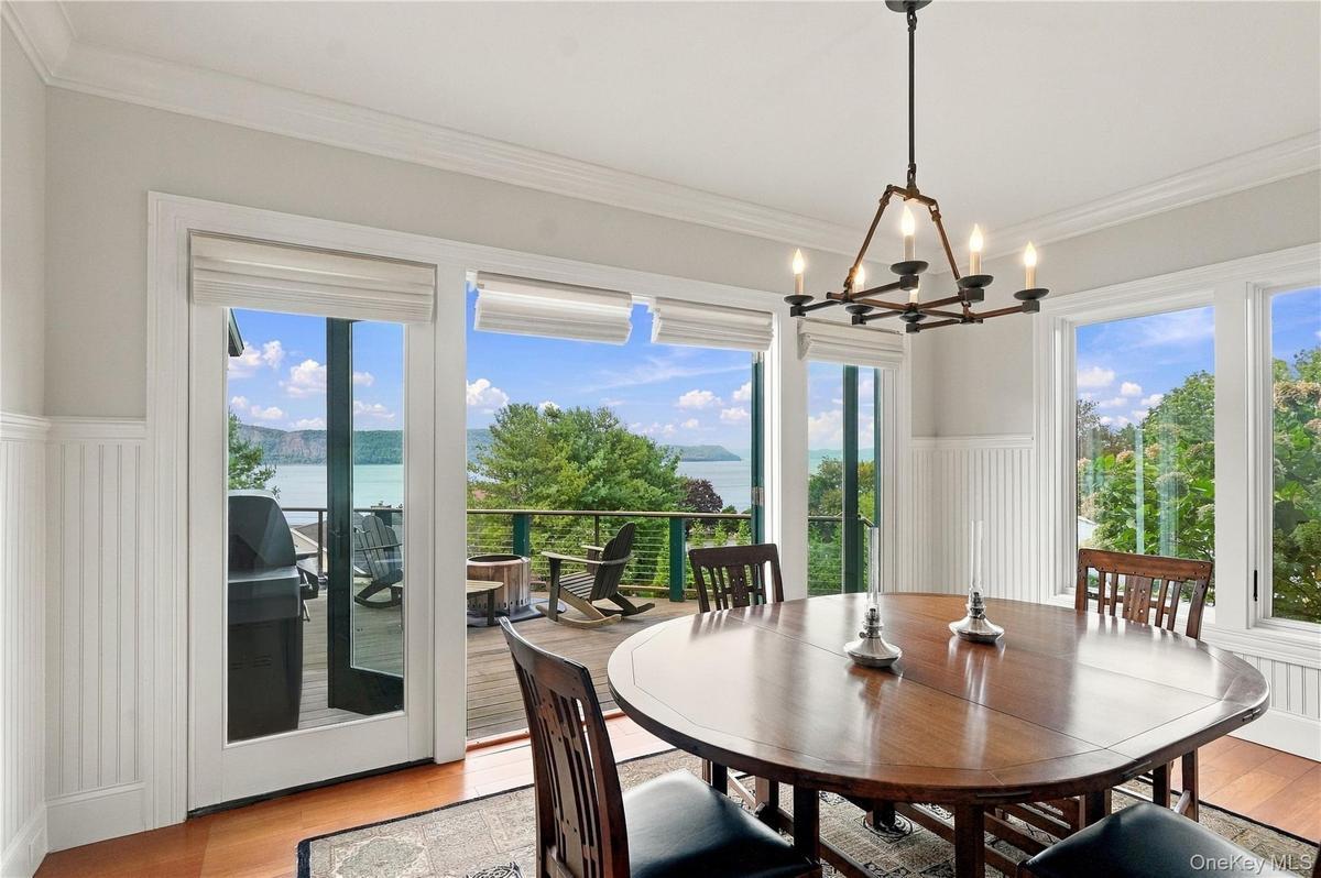 An oversized breakfast room surrounded by walls of glass, offering breathtaking Hudson River views and direct access to the expansive outdoor deck. Th