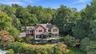 An impressive aerial view showcasing the home's striking architecture, expansive Ipe wood deck, covered outdoor lounge, and lush surrounding landscape