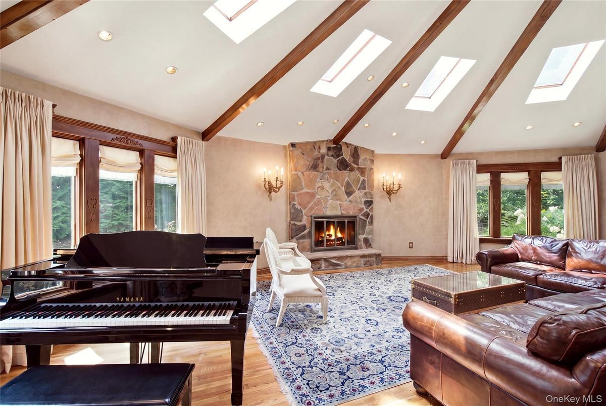 Vaulted ceiling with exposed wood beams, multiple skylights, stone-clad fireplace, and hardwood flooring