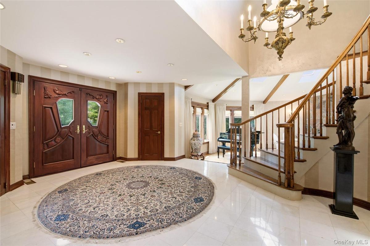 Grand entry with custom carved double doors, marble flooring, a curved staircase with wood balusters.