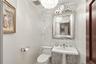 Pedestal sink with chrome fixtures, decorative wall-mounted mirror, patterned accent wall, and ceiling-mounted light fixture