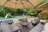 Paver patio with multiple shade umbrellas, a swimming pool with an attached slide, and a tennis court