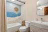 Bathtub with a mosaic-tiled accent wall, vanity with an integrated sink, and a wall-mounted mirror