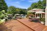 Multi-level wood deck with a built-in pergola ample seating areas, and a visible swimming pool surrounded by mature trees