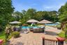 Expansive paver patio with an in-ground swimming pool, mature perimeter landscaping, and a fenced tennis court