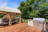 Expansive wood-finish deck featuring a covered pergola, built-in outdoor kitchen with stainless steel appliances.