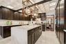 Black  oak wood cabinetry, a large center island with a waterfall countertop, tiled backsplash, coffered ceiling, and integrated stainless steel doubl