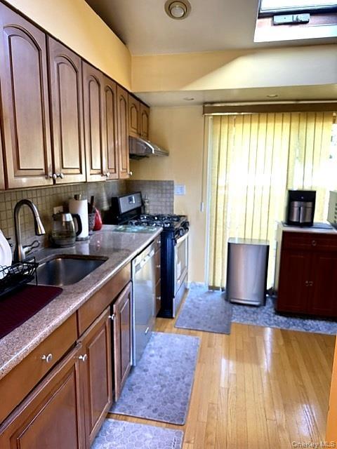 Wood-finish flooring, shaker-style cabinetry, stainless steel appliances, a tile backsplash, and a skylight