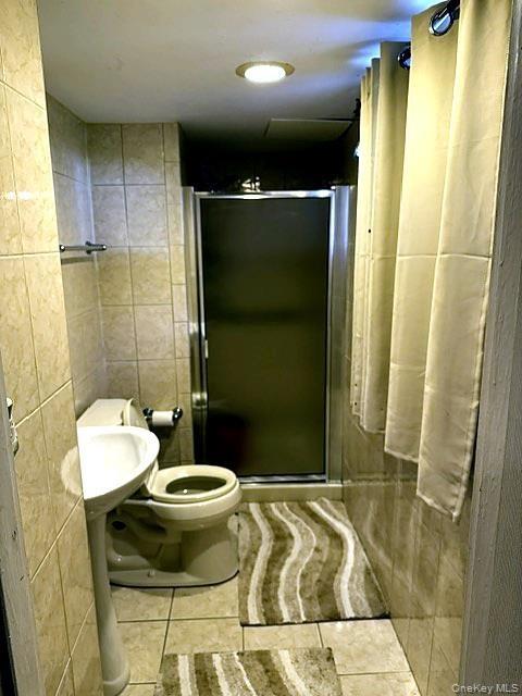 Tiled bathroom featuring a pedestal sink, toilet, and a glass-enclosed shower
