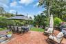 Expansive backyard featuring a red brick patio, a manicured lawn, and mature perimeter trees